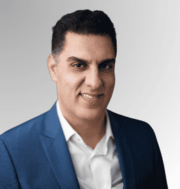 Man with short dark hair wearing a blue suit jacket and white shirt, smiling at the camera against a plain light background.