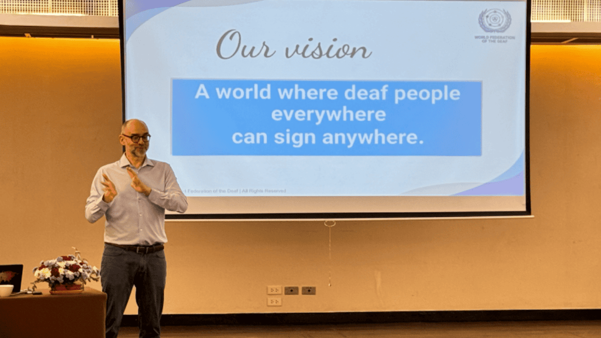 Man signing in front of a presentation slide that reads: "A world where deaf people everywhere can sign anywhere.
