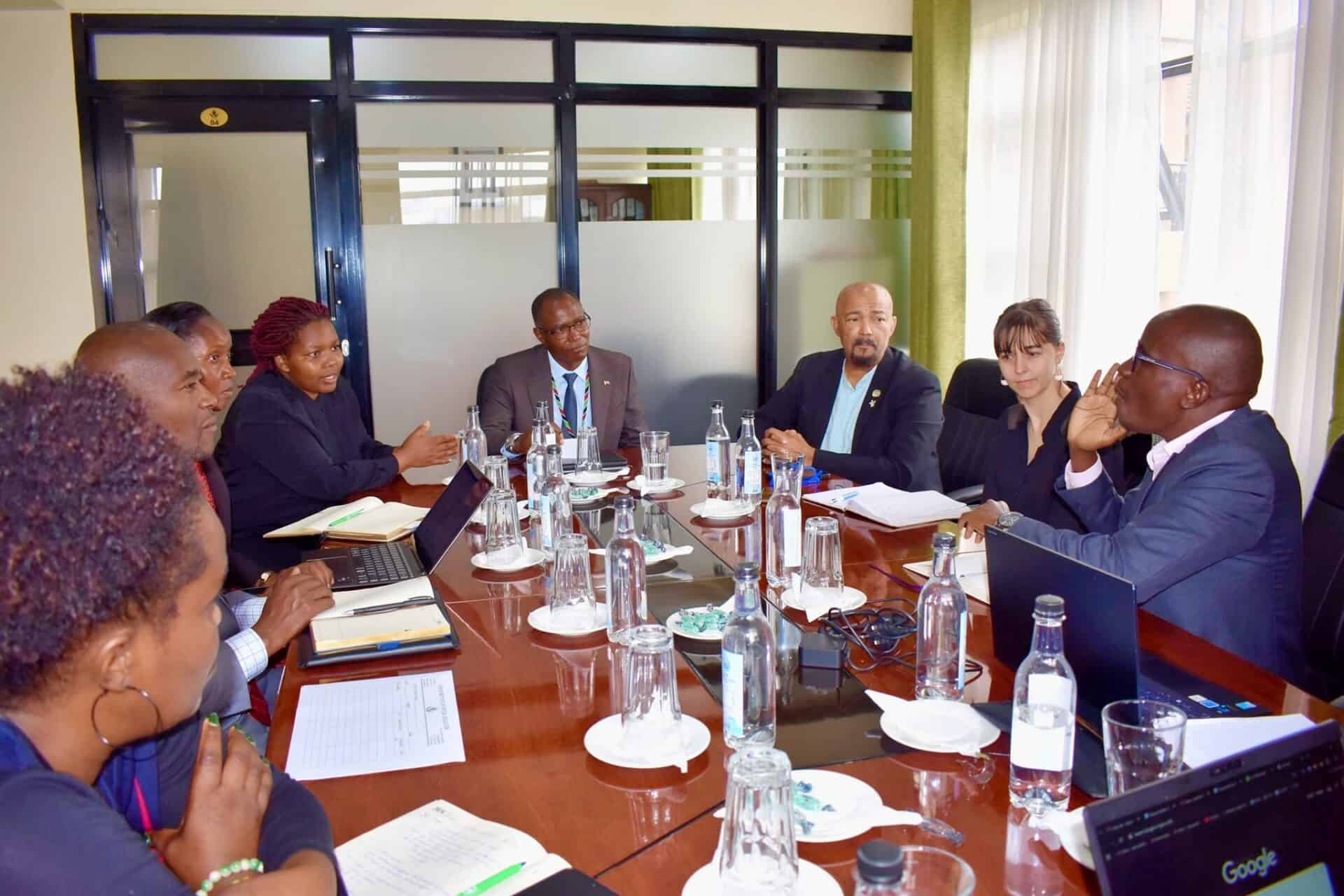 A group of professionals sits around a conference table engaged in a business meeting, with documents, laptops, and water bottles on the table.