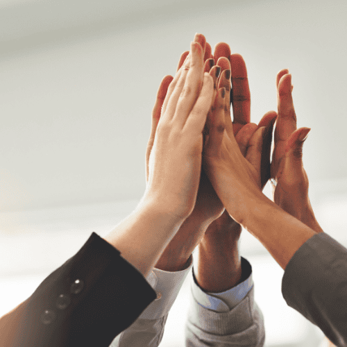 A group of people in business attire giving a group high five, with their hands joined together in the center.