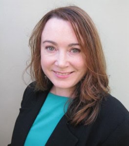 Woman with shoulder-length brown hair, wearing a teal top and black blazer, smiling against a light background.