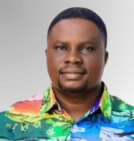 A man with short hair and a trimmed beard wearing a colourful, patterned button-up shirt, standing against a plain gradient background.