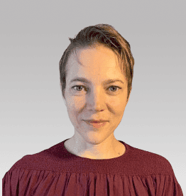 A person with short hair smiles, wearing a maroon top against a gray background.