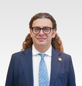 A man with long curly hair wearing glasses and a suit