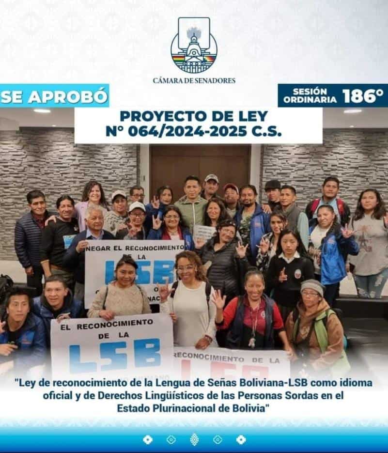 A group of people poses indoors holding signs supporting the recognition of Bolivian Sign Language as an official language, during a legislative session in Bolivia.