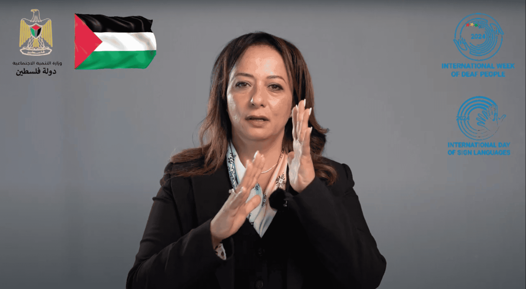 A woman in a black blazer signs in front of a gray background, next to the Palestinian flag and logos for the International Week of Deaf People and International Day of Sign Languages.