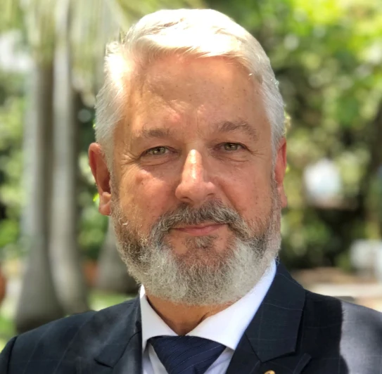 A bearded man in a suit poses outdoors, with trees blurred in the background.