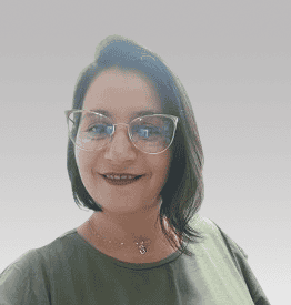 A woman with short dark hair, wearing glasses and a green top, smiles in front of a plain light gray background.