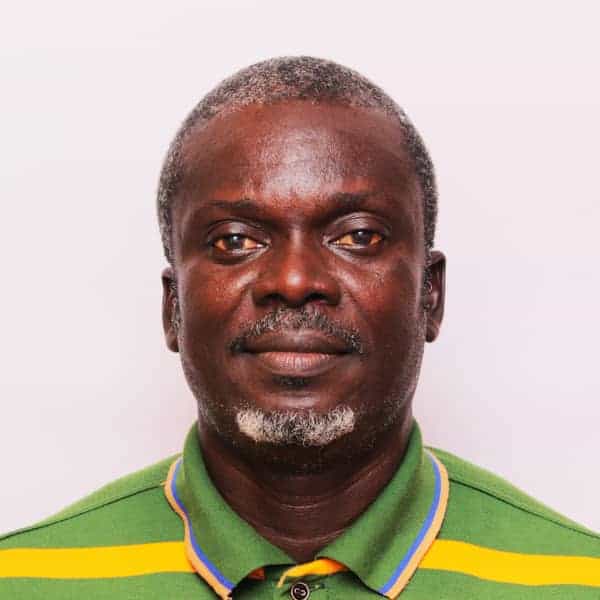 A man with short gray hair and a beard is wearing a green shirt with yellow and blue stripes, posing against a plain white background.