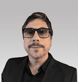 Man with short hair, beard, and glasses, wearing a black jacket, against a neutral background.