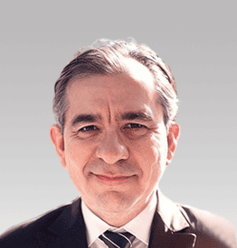 A man in a suit and tie smiles at the camera against a plain background.