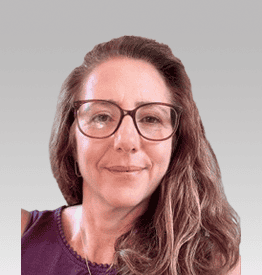 Woman with long hair and glasses, wearing a purple top, against a gray background.