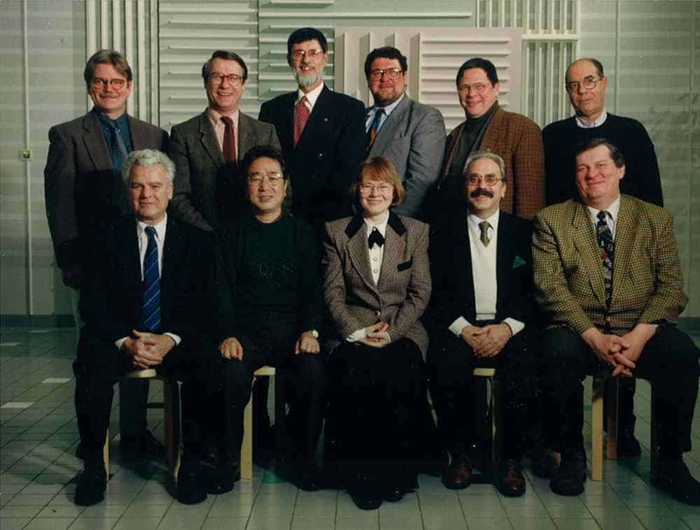 A group photo of eleven people, standing and seated, in formal attire in an indoor setting.