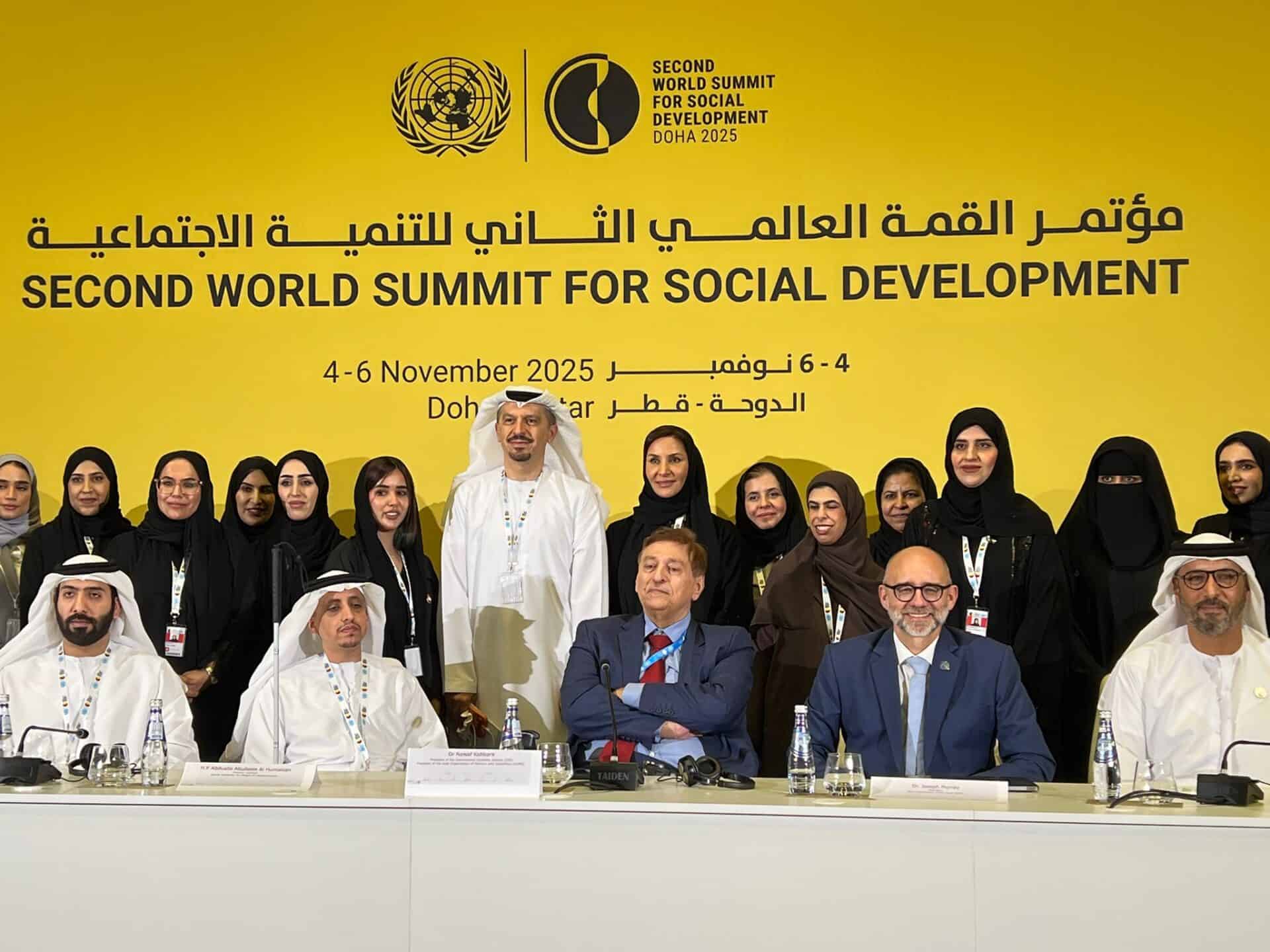 A group of men and women pose for a photo at the Second World Summit for Social Development in Doha, with a yellow event banner in the background.