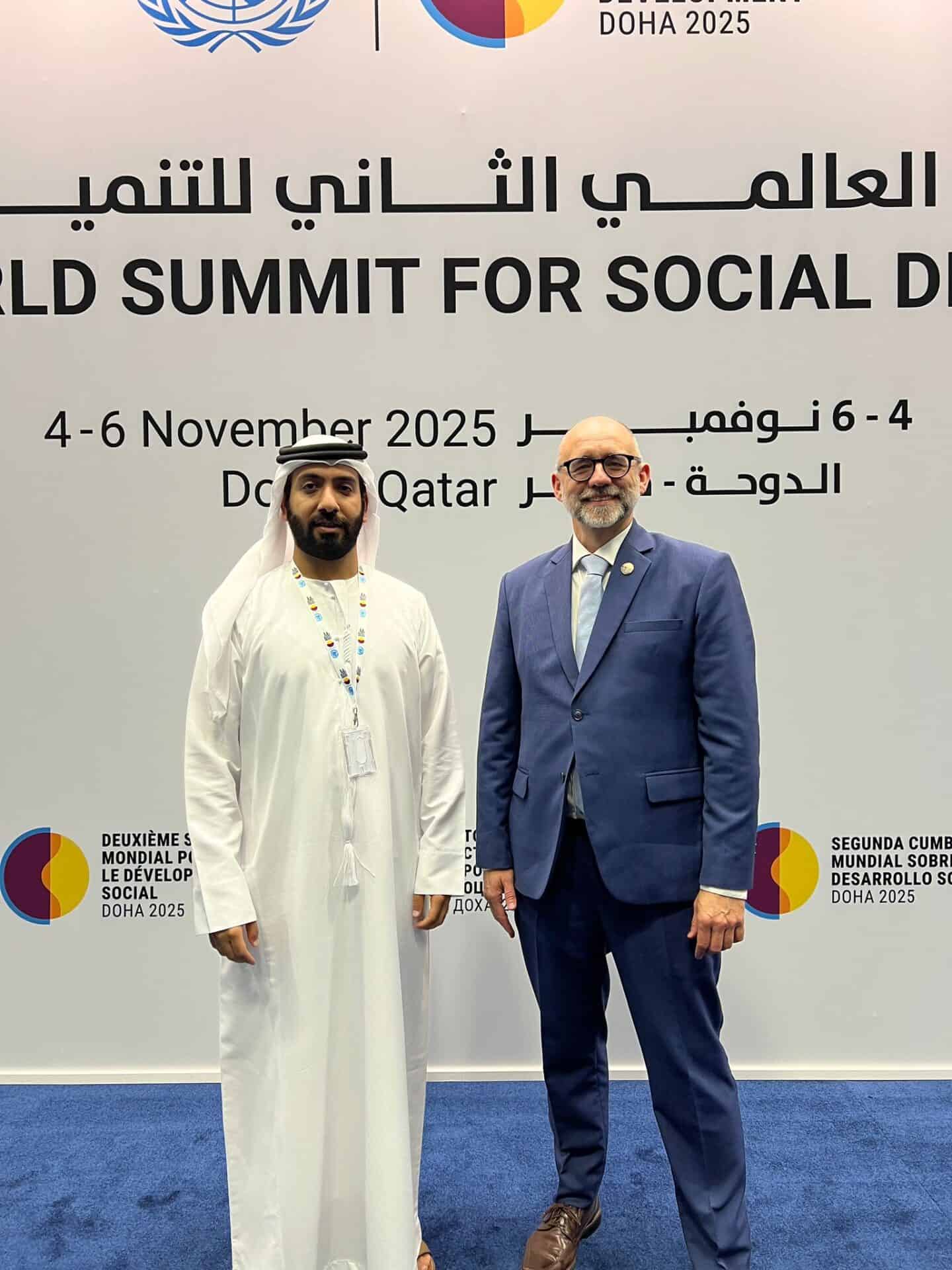 Two men pose for a photo in front of a banner for the World Summit for Social Development, scheduled for 4-6 November 2025 in Doha, Qatar.