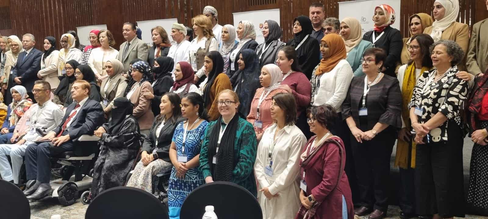A large group of people, mostly women, pose together for a group photo indoors at what appears to be a formal event or conference.