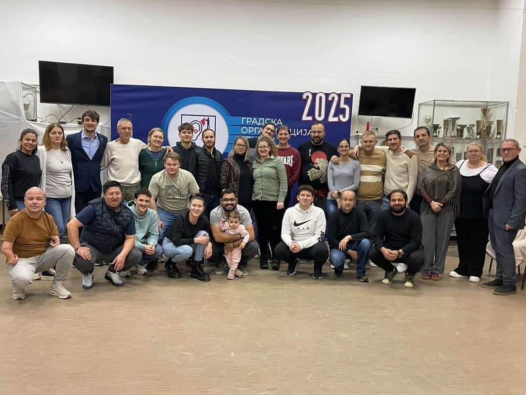 A group of about 30 people pose together indoors in front of a blue banner with "2025" written on it.