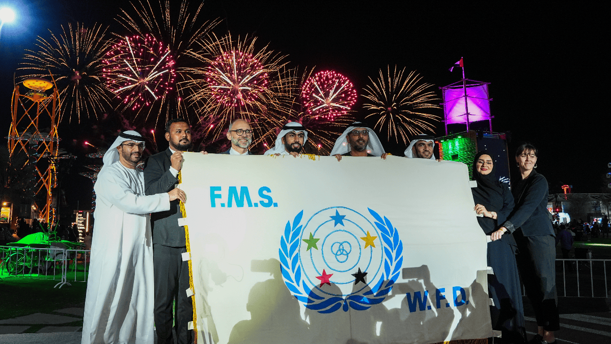Group of people holding an F.M.S. W.F.D. banner in front of colorful fireworks at night.