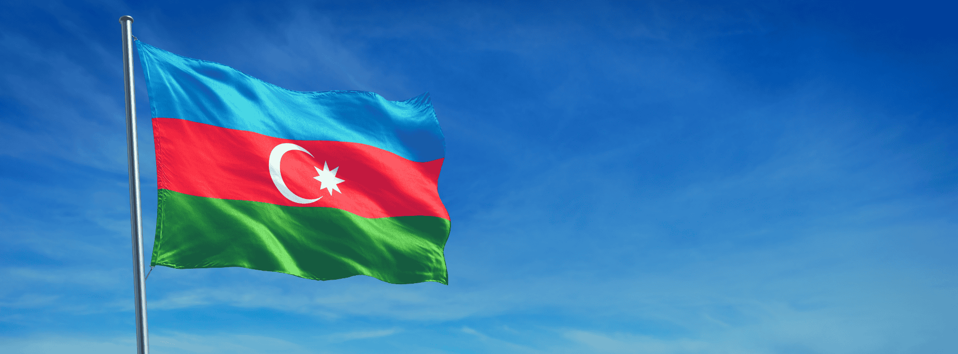 The national flag of Azerbaijan, featuring blue, red, and green horizontal stripes with a white crescent and eight-pointed star, flies against a clear blue sky.