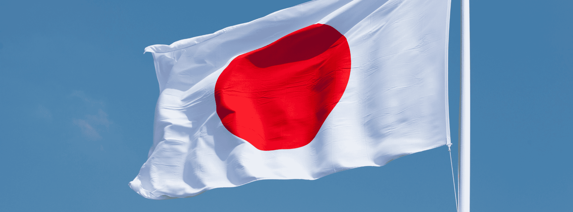 The national flag of Japan, featuring a red circle centered on a white field, is flying against a clear blue sky.