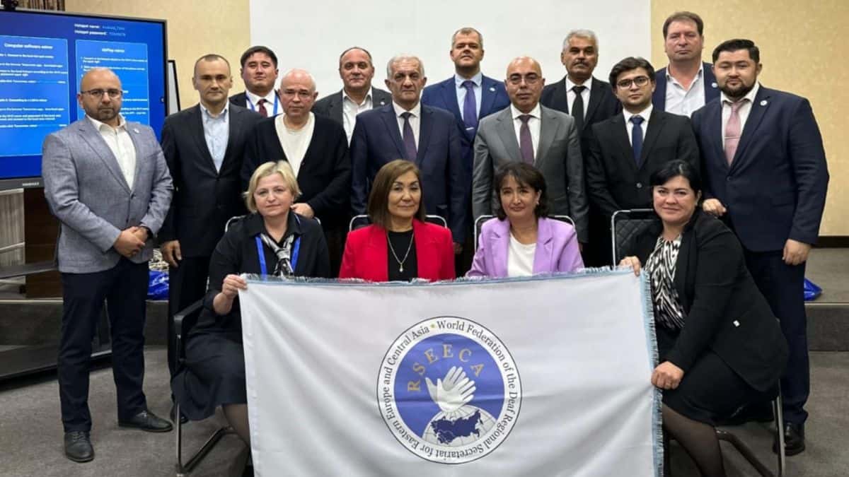 A group of people stand posing with a banner that reads "FSEA." A presentation screen is visible in the background.