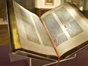 An open ancient book displayed in a glass case, with visible text in two columns on each page.